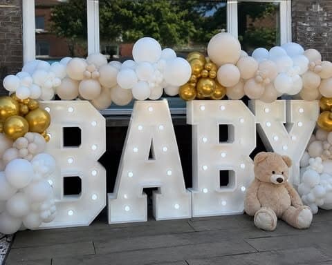 Illuminated marquee letters styled with cream balloons and soft florals for a baby shower