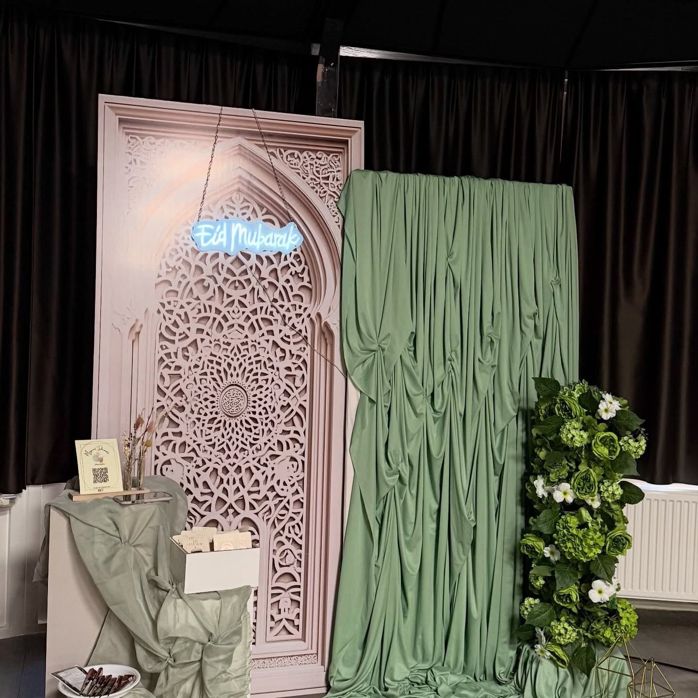 Eid Mubarak neon sign suspended over an ornate Moroccan arch print backdrop with sage green drapery and a green floral column