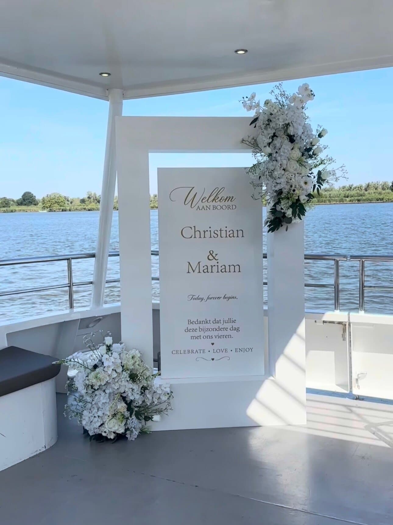 White welcome board reading Christian and Mariam, adorned with orchids and roses, aboard a wedding boat on a Dutch river