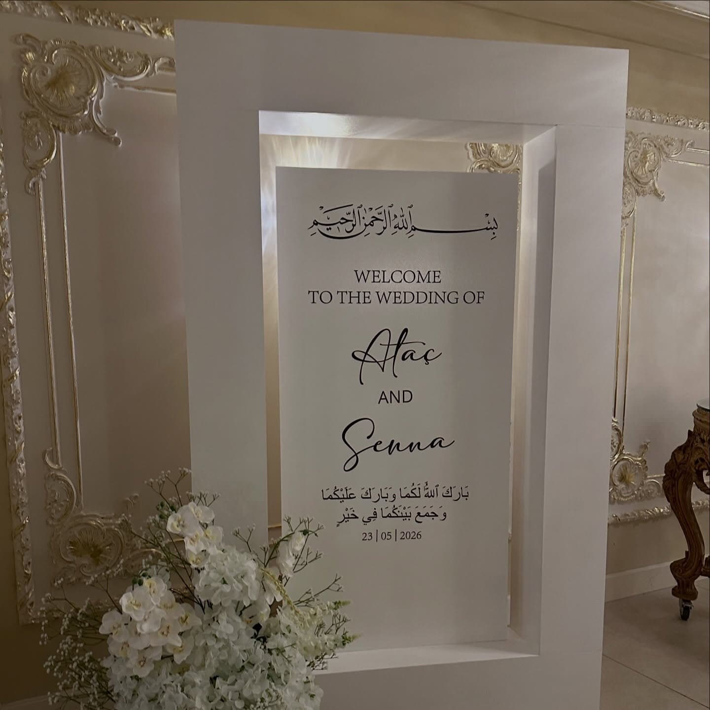 Framed wedding welcome sign with Arabic calligraphy and the couple's names in fine script, set within a gilded interior