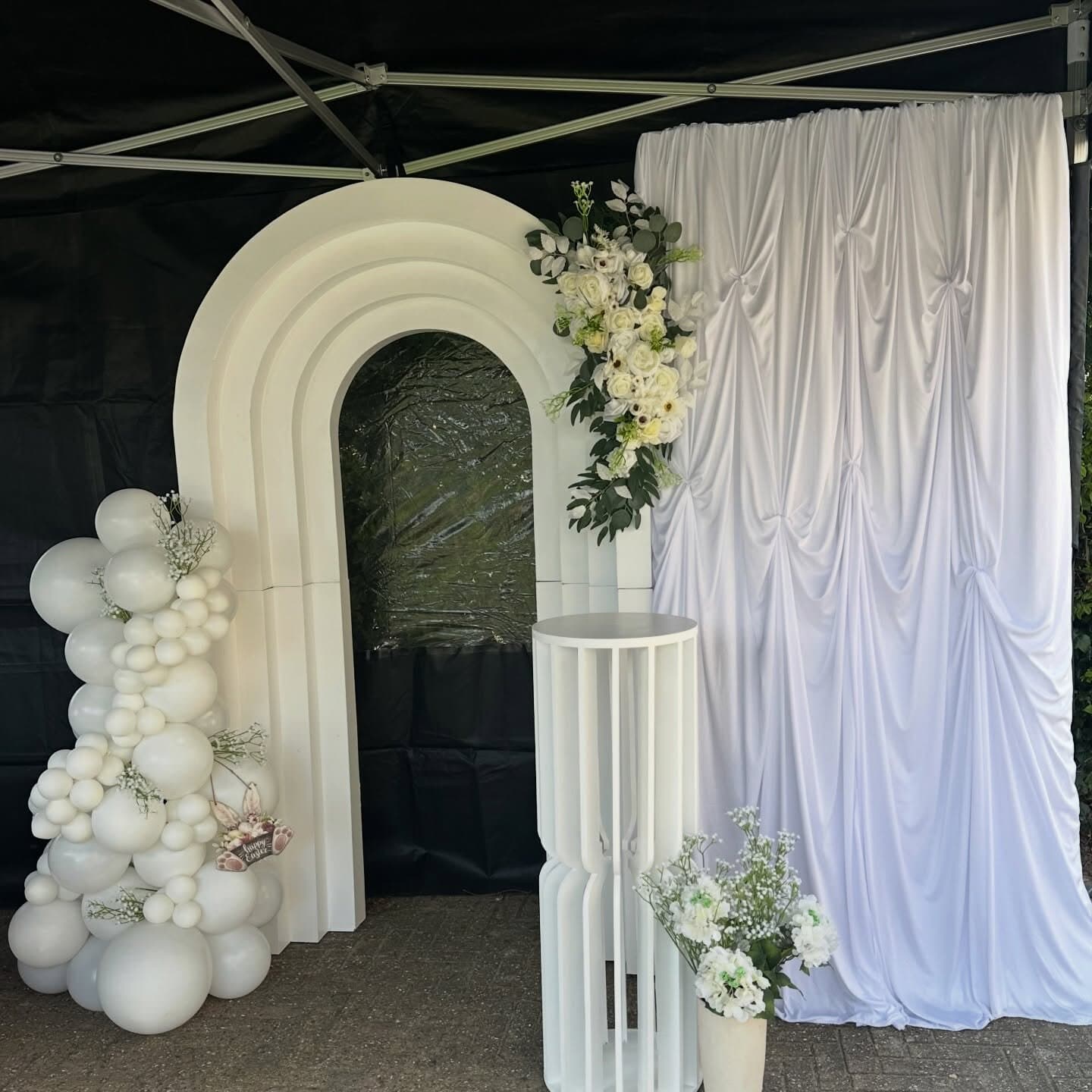 White scalloped wedding arch with an ivory balloon garland, silk drapery backdrop and fluted plinth